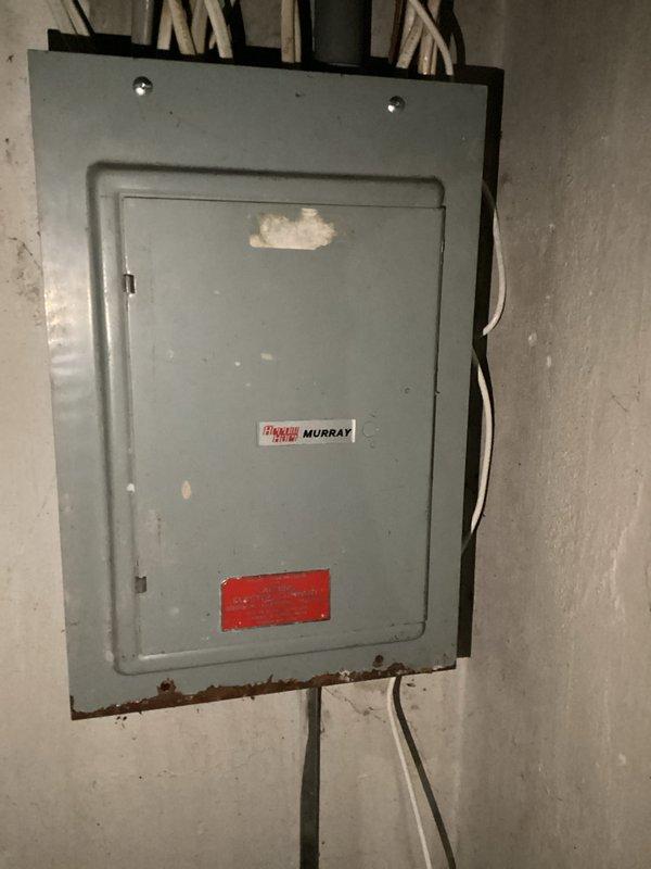 Completed electrical club inspection of Murray/Crouse-Hinds main service panel in basement utility area. Documented existing conditions including significant rust corrosion along bottom edge of panel enclosure indicating moisture intrusion, deteriorated paint on panel door, aging circuit breaker configuration with dual vertical rows, and multiple handwritten markings on equipment surfaces. Photographed all electrical connections, conduit entries at top and bottom of panel, adjacent junction box with posted documentation, and overall panel installation for compliance review and future reference.