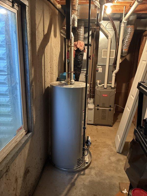 Completed full water heater installation in basement utility room. Removed existing unit and installed new tall cylindrical water heater with proper venting connections to existing ductwork system. Connected copper supply lines with red-handled isolation valves for system control and installed blue expansion tank on wall for thermal expansion protection. Verified all plumbing connections, tested pressure relief valve operation, and ensured proper clearances from furnace and other mechanical equipment. System tested and operational.