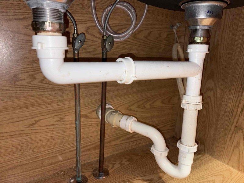 Responded to kitchen sink leak complaint. Upon arrival, inspected double-basin stainless steel sink with modern faucet assembly and spray nozzle attachment. Examined visible moisture and water droplets on sink surface. Accessed cabinet beneath sink to evaluate plumbing system, including white PVC drain assemblies, P-trap configuration, and braided stainless steel supply lines. Inspected metal drain baskets, threaded tailpieces, and slip joint connections for signs of leakage or deterioration. Documented existing plumbing configuration with photographs for service records. All accessible plumbing components assessed for proper function and potential leak sources.