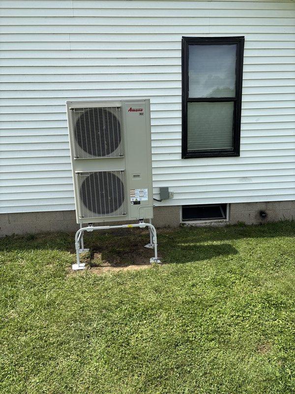 Completed full HVAC system installation including new Amana heat pump unit and furnace. Outdoor unit mounted on elevated white metal stand with proper clearances from structure, electrical disconnect installed per code. Indoor furnace positioned in mechanical room with new air filter housing, PVC venting routed to exterior, and all ductwork connections completed. System tested and operational.