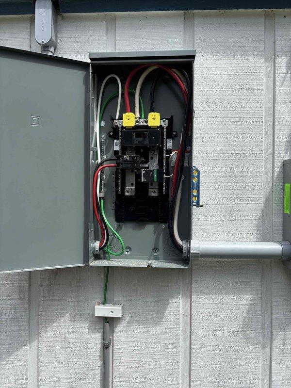 Completed 200-amp electrical service upgrade on residential structure with white horizontal siding. Coordinated utility disconnect and reconnect with power company to facilitate safe panel replacement. Installed new gray metal service panel with updated circuit breaker configuration, proper wire management including red, black, white, and green conductors, yellow wire terminals, and metallic conduit connections. Established proper grounding system with grounding wire connection to grounding rod. Obtained electrical permit and passed inspection. Power was temporarily disconnected in the morning and successfully restored in the afternoon following completion of upgrade work.