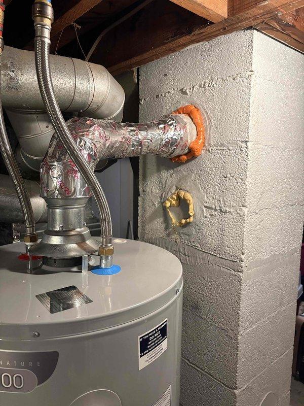 Responded to report of soot leaking from water heater vent connection at chimney entry point in eighty-year-old home, condition present for approximately seven days. Inspected atmospheric vent water heater installation, vent pipe connections, and chimney penetration point; documented existing conditions with photographs of mechanical room installation and exterior chimney structure with cap. Identified improper venting condition causing combustion byproduct spillage at chimney interface requiring corrective action to ensure safe operation and proper draft.