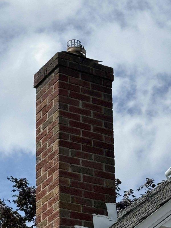 Responded to report of soot leaking from water heater vent connection at chimney entry point in eighty-year-old home, condition present for approximately seven days. Inspected atmospheric vent water heater installation, vent pipe connections, and chimney penetration point; documented existing conditions with photographs of mechanical room installation and exterior chimney structure with cap. Identified improper venting condition causing combustion byproduct spillage at chimney interface requiring corrective action to ensure safe operation and proper draft.