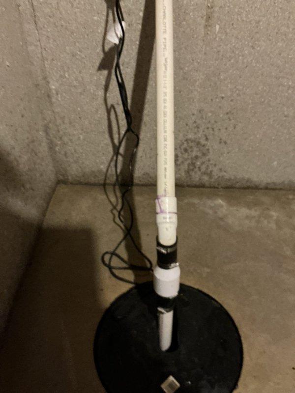 Responded to emergency call for sump pump failure causing basement flooding. Upon arrival, water mitigation team had already extracted standing water from the affected area. Inspected sump pump system including vertical PVC discharge pipe, base plate assembly, and electrical connections. Documented existing conditions showing white PVC discharge pipe with multiple securing points extending from floor-mounted black base plate to ceiling level, with electrical wiring present. Assessed pump functionality and drainage system to identify cause of flooding incident and ensure proper operation restored to prevent further water intrusion.