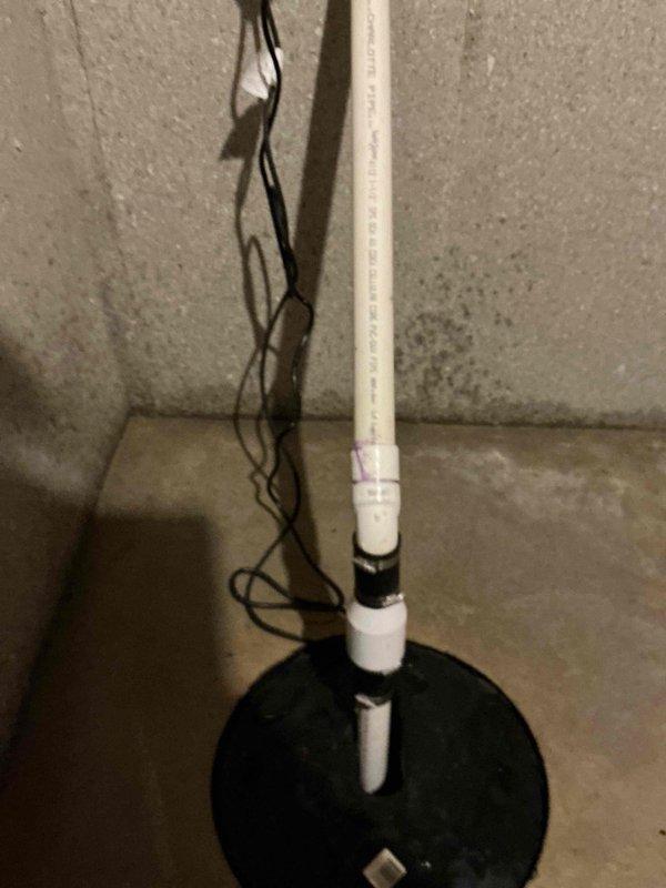Responded to emergency call for sump pump failure causing basement flooding. Upon arrival, water mitigation team had already extracted standing water from the affected area. Inspected sump pump system including vertical PVC discharge pipe, base plate assembly, and electrical connections. Documented existing conditions showing white PVC discharge pipe with multiple securing points extending from floor-mounted black base plate to ceiling level, with electrical wiring present. Assessed pump functionality and drainage system to identify cause of flooding incident and ensure proper operation restored to prevent further water intrusion.