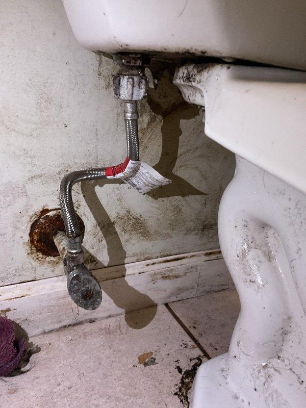 # Toilet Base Leak Repair

Responded to service call for toilet leaking at base during each flush cycle. Upon inspection, found extensive water damage and rust staining on floor tiles surrounding toilet base, indicating prolonged leak condition. Examined toilet tank interior and identified aged, worn flapper valve with visible deterioration and significant mineral deposits throughout tank components. Assessed braided stainless steel supply line connection and mounting hardware for proper seal integrity. Documented existing conditions including heavy mineral buildup on fill valve assembly, darkened water in tank, and compromised wax ring seal at toilet base. Photographed plumbing connections, floor damage patterns, and internal tank components showing hard water accumulation and component wear on Gerber brand toilet. Recommended wax ring replacement and flapper valve service to resolve active leak issue.