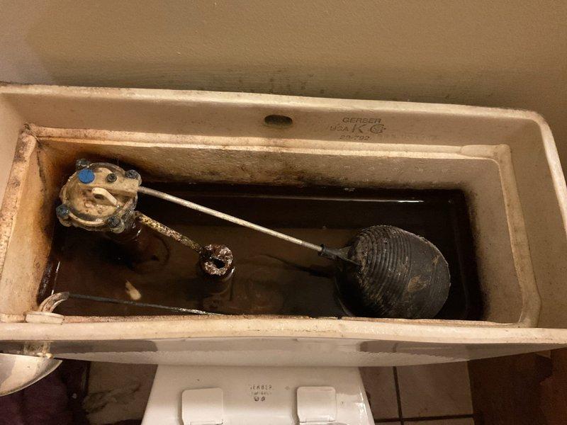 # Toilet Base Leak Repair

Responded to service call for toilet leaking at base during each flush cycle. Upon inspection, found extensive water damage and rust staining on floor tiles surrounding toilet base, indicating prolonged leak condition. Examined toilet tank interior and identified aged, worn flapper valve with visible deterioration and significant mineral deposits throughout tank components. Assessed braided stainless steel supply line connection and mounting hardware for proper seal integrity. Documented existing conditions including heavy mineral buildup on fill valve assembly, darkened water in tank, and compromised wax ring seal at toilet base. Photographed plumbing connections, floor damage patterns, and internal tank components showing hard water accumulation and component wear on Gerber brand toilet. Recommended wax ring replacement and flapper valve service to resolve active leak issue.