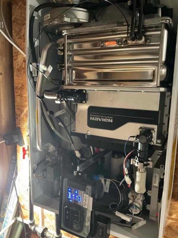 Responded to service call for ongoing water heater issues with 8-year-old Navien tankless unit. Inspected wall-mounted system including heat exchanger assembly, circulation pump, gas valve, and digital control panel. Documented internal mechanical components and operational status of unit with photos showing all major connections, plumbing interfaces, and electrical wiring in proper working condition.