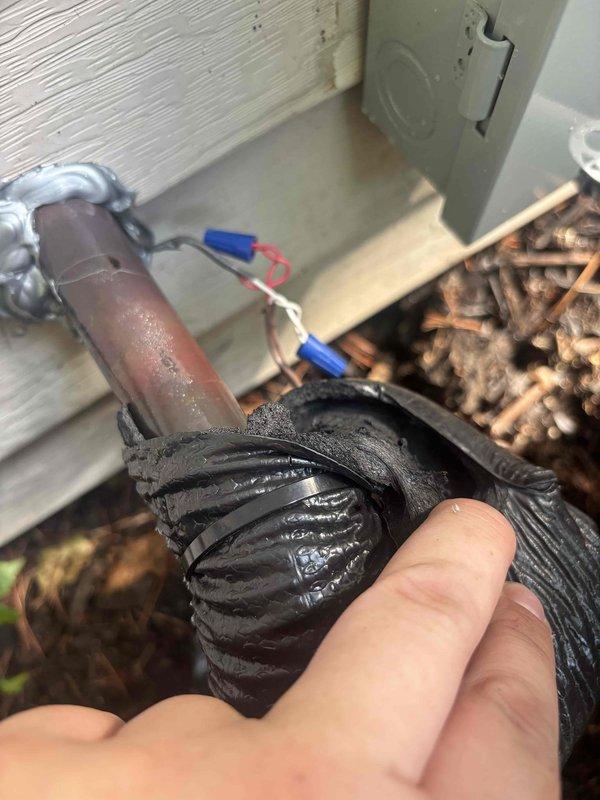 Responded to service call for HVAC unit producing loud noise during operation. Upon inspection, discovered severely deteriorated flex conduit and significant debris accumulation around outdoor unit components. The corrugated rubber hose showed advanced wear and surface degradation, while copper refrigerant lines displayed normal oxidation patina. Found extensive organic debris including dried plant material, twigs, and mulch accumulated in equipment base, restricting airflow and contributing to operational noise. Electrical connections with wire nuts were inspected and found secure. Removed debris buildup from unit base and surrounding area. Documented equipment condition with photographs showing weathered components and rust on metal housing. Unit cooling function confirmed operational with no refrigerant issues detected. Recommended replacement of deteriorated flex conduit to prevent future problems and advised regular debris removal to maintain proper airflow and quiet operation.