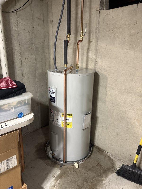 Successfully completed installation of new Carrier HVAC system and residential water heater in basement utility area. The HVAC installation included proper mounting of furnace unit with air handler, installation of PVC venting pipes, and electrical conduit connection. The water heater replacement involved installing a new white cylindrical unit with copper supply piping, brass fittings, and flexible conduit for electrical connection. Both units were positioned against concrete walls on concrete flooring, with all connections properly secured and tested for operation.