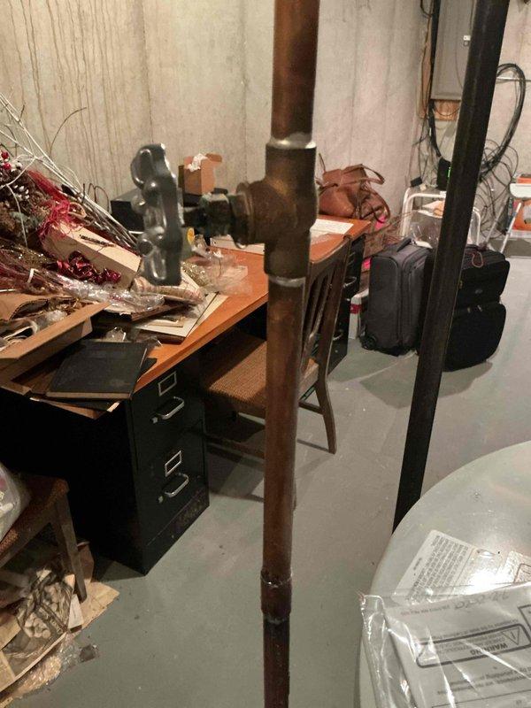Responded to non-emergency plumbing leak in 26-year-old residential property that had been dripping for approximately 4-5 days. Upon arrival, located the source of the leak at a vertical copper pipe assembly in the basement utility area. The pipe displayed age-appropriate patina and weathering consistent with the home's age. Inspected the valve junction near the upper portion of the pipe run where moisture was present. Documented the condition of the affected plumbing system and surrounding area with photographic evidence, noting water staining on adjacent concrete block walls indicative of ongoing moisture exposure. Assessed the integrity of the copper piping system and valve assembly to determine appropriate repair methodology. The leak was isolated and repair recommendations were provided to address the dripping condition and prevent further water damage to the basement area.