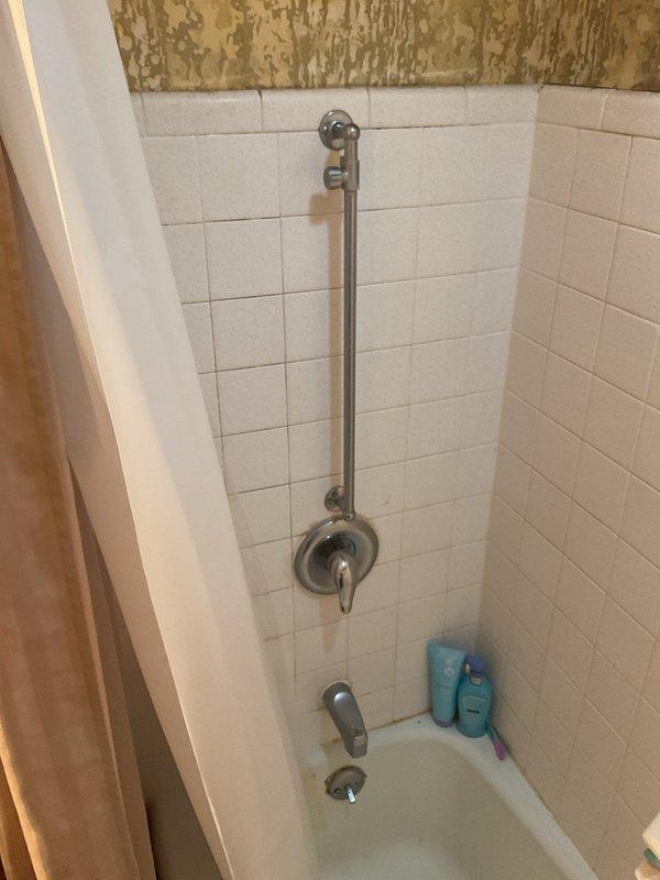 Conducted on-site assessment for tub-shower replacement project. Documented existing bathroom conditions, including white square-tiled shower surround with chrome fixtures, standard alcove-style bathtub, and significant wall deterioration above tile line with extensive peeling and flaking of upper wall surfaces. Photographed current installation to provide comprehensive quote for new tub-shower unit replacement.