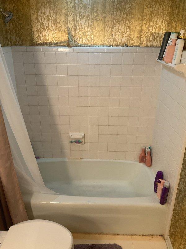 Conducted on-site assessment for tub-shower replacement project. Documented existing bathroom conditions, including white square-tiled shower surround with chrome fixtures, standard alcove-style bathtub, and significant wall deterioration above tile line with extensive peeling and flaking of upper wall surfaces. Photographed current installation to provide comprehensive quote for new tub-shower unit replacement.