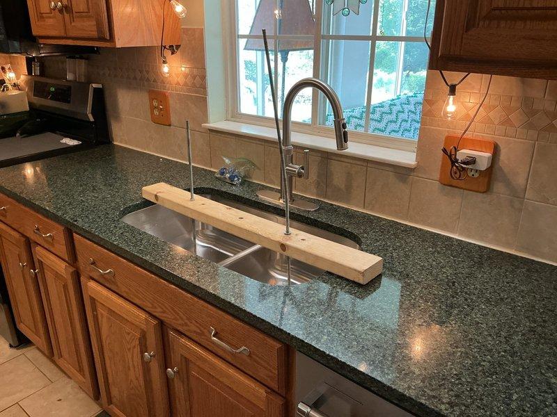 Completed undermount double-basin stainless steel sink installation in existing dark granite countertop. Installed modern gooseneck faucet with pull-down spray head in chrome finish, connected water supply lines, and verified proper drainage function on both basin assemblies. All plumbing connections tested and confirmed leak-free upon completion.
