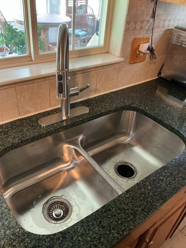 Completed undermount double-basin stainless steel sink installation in existing dark granite countertop. Installed modern gooseneck faucet with pull-down spray head in chrome finish, connected water supply lines, and verified proper drainage function on both basin assemblies. All plumbing connections tested and confirmed leak-free upon completion.