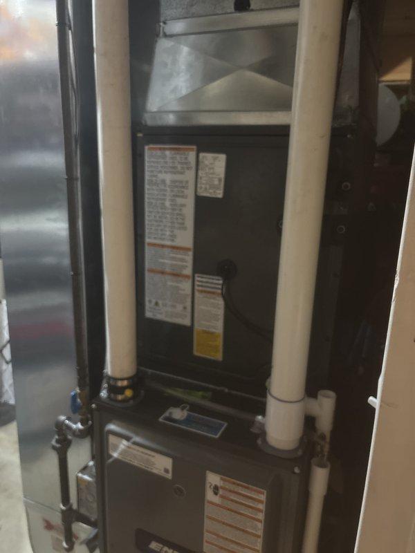 Completed same-day installation of complete HVAC system including indoor furnace unit and outdoor air conditioning condenser. Indoor unit installed in basement/utility room with proper PVC venting system, gas line connection with shutoff valve, and integrated ductwork with metallic plenum transition. Outdoor condenser unit positioned on concrete pad against building exterior with appropriate clearances, electrical disconnect box mounted on siding, and refrigerant lines properly connected between indoor and outdoor components.