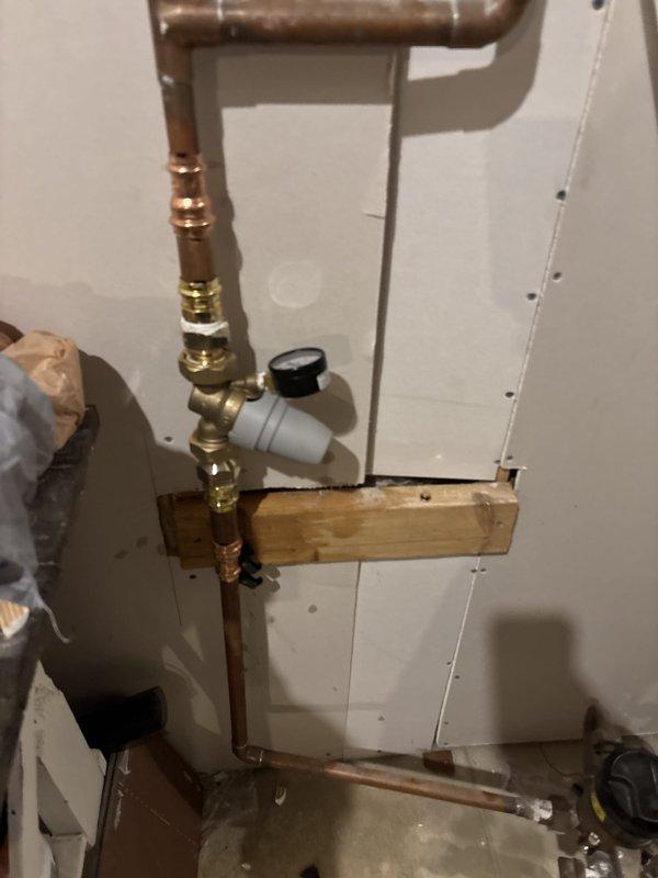 Completed full water heater installation in utility area with new copper supply piping, brass shut-off valves, pressure relief valve assembly with gauge, and proper mounting hardware. Installed vertical copper supply lines with compression fittings and 90-degree elbows, secured plumbing components to wall-mounted wooden backing board for structural support, and integrated PVC drainage/vent piping. All connections tested and verified operational with no leaks detected.