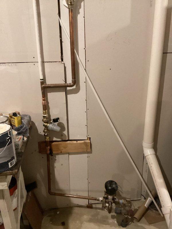 Completed full water heater installation in utility area with new copper supply piping, brass shut-off valves, pressure relief valve assembly with gauge, and proper mounting hardware. Installed vertical copper supply lines with compression fittings and 90-degree elbows, secured plumbing components to wall-mounted wooden backing board for structural support, and integrated PVC drainage/vent piping. All connections tested and verified operational with no leaks detected.