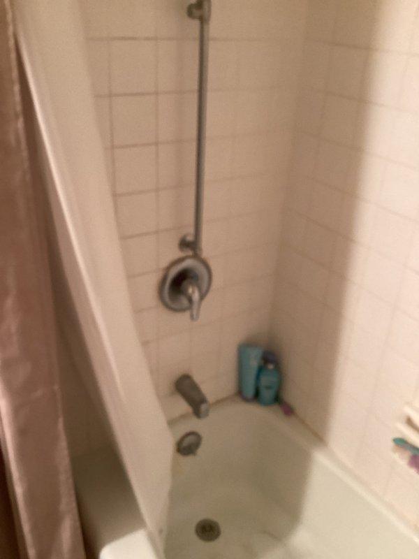 Conducted on-site assessment for tub-shower replacement estimate in residential bathroom. Documented existing alcove-style white bathtub with standard chrome fixtures including wall-mounted shower valve, tub spout, and vertical supply pipe, along with white subway tile surround. Photographed current bathroom configuration including vanity area to provide comprehensive quote for new tub-shower installation.