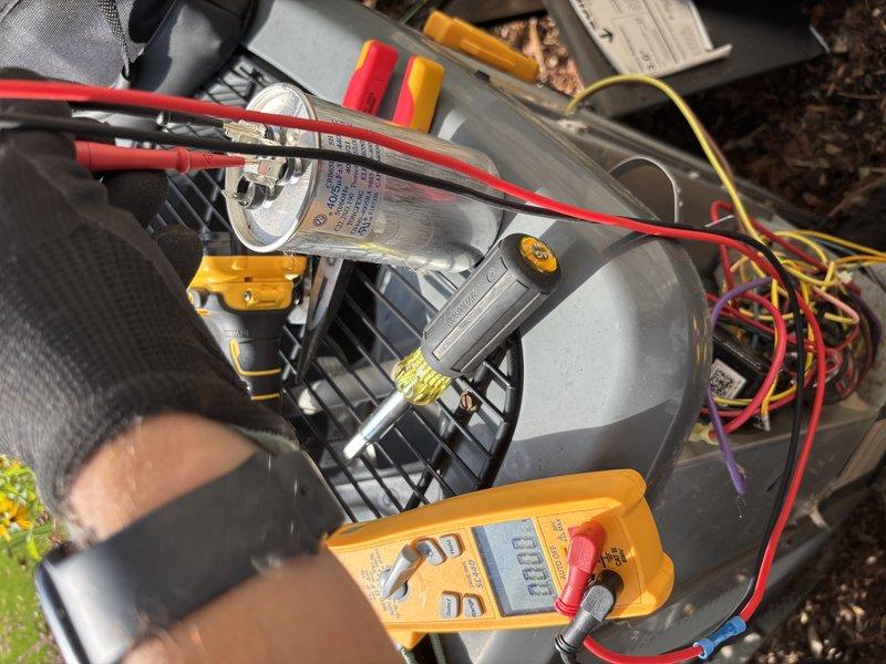 Completed annual cooling maintenance on 6-year-old EnergiAir heat pump system. Performed electrical diagnostics using digital multimeter to test capacitor function and verify proper voltage readings at all terminals. Removed significant accumulation of leaves, organic debris, and dirt from internal components and around capacitor assembly to restore proper airflow and prevent potential electrical issues. Inspected all wire connections including red, yellow, purple, and orange leads for secure termination and signs of wear. Verified system operation and documented equipment condition with photos for service records.