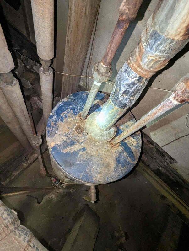 # Water Heater Replacement Estimate

Evaluated 16-year-old water heater with pilot valve assembly determined to be beyond economical repair due to extensive corrosion throughout the unit and connecting plumbing components. Documented severe deterioration including corroded blue tank housing, rusted pipe connections, and degraded insulation materials. Assessed installation location constraints and identified potential venting challenges for conventional tank-type replacement due to confined basement space configuration. Provided estimate options for both traditional tank water heater and tankless alternatives to address customer's need for compact hot water solution. Recommended tankless system as preferred option to overcome existing venting limitations and spatial restrictions in current installation area.