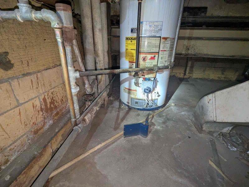 # Water Heater Replacement Estimate

Evaluated 16-year-old water heater with pilot valve assembly determined to be beyond economical repair due to extensive corrosion throughout the unit and connecting plumbing components. Documented severe deterioration including corroded blue tank housing, rusted pipe connections, and degraded insulation materials. Assessed installation location constraints and identified potential venting challenges for conventional tank-type replacement due to confined basement space configuration. Provided estimate options for both traditional tank water heater and tankless alternatives to address customer's need for compact hot water solution. Recommended tankless system as preferred option to overcome existing venting limitations and spatial restrictions in current installation area.
