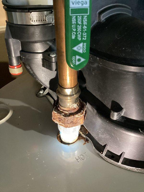 Responded to inspection request for rusting connection on recently installed standard tank water heater. Upon arrival, performed thorough visual inspection of the water heater and associated plumbing connections. Identified significant corrosion and oxidation on copper pipe threaded connection at hot water circulation pump interface, with heavy greenish-brown patina and mineral deposit buildup at the joint where copper pipe meets white plastic fitting. Documented the deteriorated connection showing crusty buildup and severe oxidation at the threaded joint area. Photographed all affected components including the black circulation pump system, corroded copper piping, and overall water heater installation for warranty documentation and follow-up with original installer. Inspection revealed corrosion isolated to specific connection point on hot water side of system.