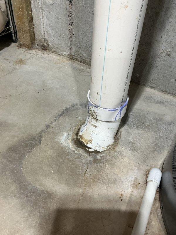Broke out concrete floor to access and replace deteriorated drain fitting at base of vertical PVC drain line. Removed damaged fitting showing signs of corrosion and staining, installed new PVC fitting with proper connections, and secured pipe assembly with metal clamp. Completed work in 3 hours with photo documentation of installation.
