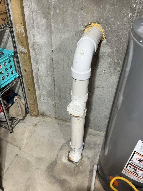 Broke out concrete floor to access and replace deteriorated drain fitting at base of vertical PVC drain line. Removed damaged fitting showing signs of corrosion and staining, installed new PVC fitting with proper connections, and secured pipe assembly with metal clamp. Completed work in 3 hours with photo documentation of installation.