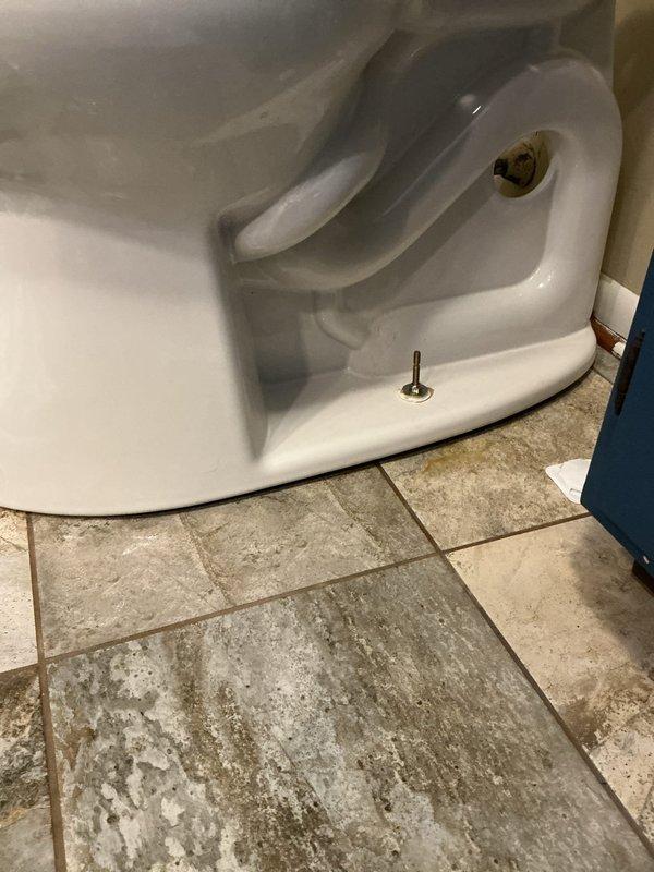Responded to ongoing toilet issue at 50-year-old residential property. Inspected toilet installation and identified significant mineral deposits and staining on bathroom floor tiles around toilet base, along with visible mounting hardware. Documented conditions with photos showing worn flooring and accumulation of residue indicating potential leak or seepage issue requiring repair.