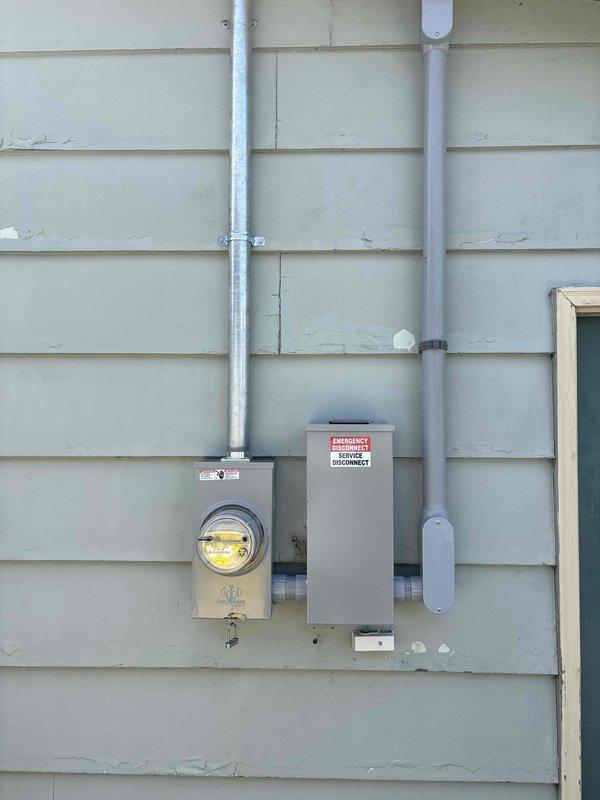Completed 200-amp electrical service upgrade on residential property. Coordinated utility disconnect and reconnect with power company, obtained electrical permit, and scheduled required inspections. Installed new meter base, service disconnect panel, and exterior conduit runs on building exterior with light-colored lap siding. All electrical components properly mounted and secured to exterior wall with appropriate hardware and weatherproof connections. Power restoration confirmed following successful completion of work and inspection approval.