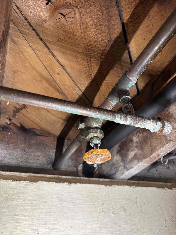 Completed annual cooling maintenance on 25-year-old Trane system. Performed comprehensive tune-up inspection including refrigerant line assessment in attic space. Inspected insulated suction line and associated plumbing infrastructure, noting aged valve assembly with significant corrosion and oxidation on handle and body. Documented condition of copper piping showing mineral deposits and patina formation, as well as galvanized piping with surface oxidation. Verified best contact number on file. System operational upon completion. Photographic documentation captured for service records.