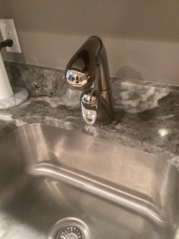 Completed faucet installation and addressed secondary faucet issue that had been present for approximately one week. Inspected under-sink plumbing configuration, which included white PVC P-trap assembly in good condition with proper drainage connections to wall outlet. Verified flexible water supply lines were properly secured and functional. Installed chrome two-handle faucet on granite countertop with stainless steel undermount sink basin. Tested water flow, checked for leaks at all connection points, and confirmed proper operation of both hot and cold water controls. All plumbing components functioning correctly upon completion.