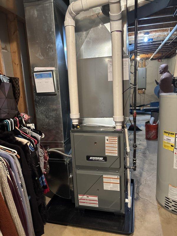 Completed full furnace installation in residential basement utility area. Installed gray metal furnace unit with proper venting system using white PVC piping with elbows and vertical runs extending from unit top. Connected all necessary ductwork including black flexible ducting to air handler, installed condensate drainage lines, and verified all manufacturer specifications and safety labels were properly affixed to equipment. System tested and operational upon completion.