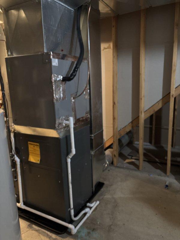 Completed full furnace installation in residential basement utility area. Installed gray metal furnace unit with proper venting system using white PVC piping with elbows and vertical runs extending from unit top. Connected all necessary ductwork including black flexible ducting to air handler, installed condensate drainage lines, and verified all manufacturer specifications and safety labels were properly affixed to equipment. System tested and operational upon completion.
