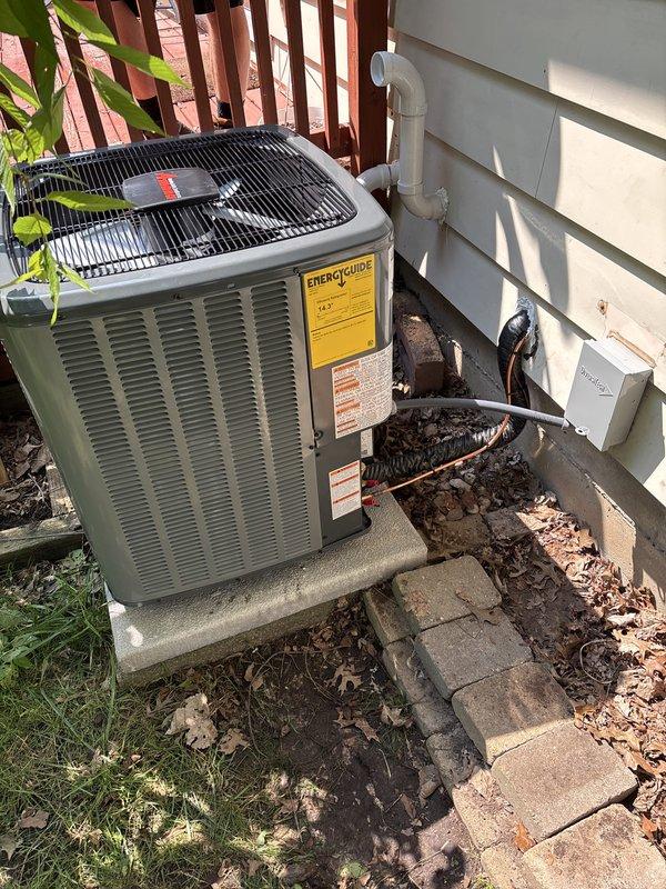 Completed full residential HVAC system installation including Amana furnace and outdoor air conditioning unit. Furnace installed in basement utility area with proper PVC venting, ductwork connections, and electrical conduit routing per manufacturer specifications. Outdoor condensing unit positioned on concrete pad adjacent to exterior wall with appropriate clearances, electrical disconnect box mounted, refrigerant lines connected, and system secured to building structure. All components properly labeled with energy guide information, tested for operation, and installation verified to meet building code requirements.