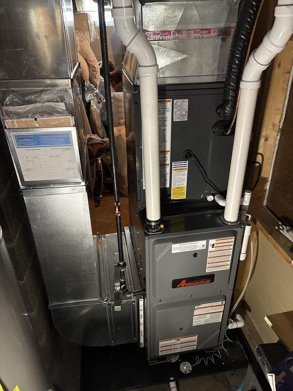 Completed full residential HVAC system installation including Amana furnace and outdoor air conditioning unit. Furnace installed in basement utility area with proper PVC venting, ductwork connections, and electrical conduit routing per manufacturer specifications. Outdoor condensing unit positioned on concrete pad adjacent to exterior wall with appropriate clearances, electrical disconnect box mounted, refrigerant lines connected, and system secured to building structure. All components properly labeled with energy guide information, tested for operation, and installation verified to meet building code requirements.