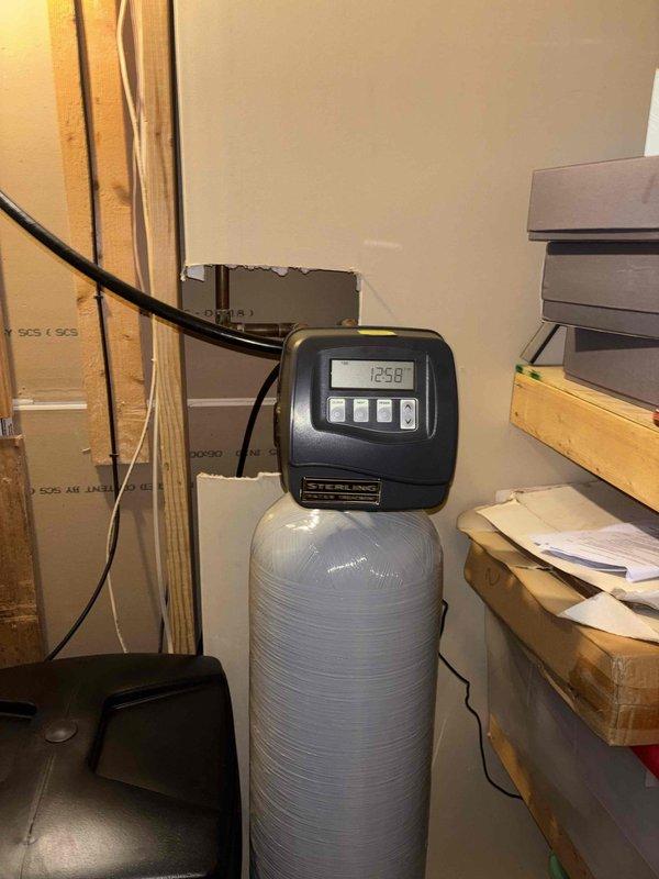 Completed installation of water heater and water softener system in utility room. Installed new water softener unit with digital control head, connected copper supply lines through wall penetration, and configured system controls for proper operation. All plumbing connections secured, system tested and verified operational with no leaks detected.
