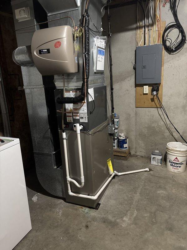 Completed full HVAC system replacement including outdoor condensing unit and indoor air handler components. New condenser installed on concrete pad with proper refrigerant line connections, electrical conduit, and drainage configuration. Indoor furnace and humidifier assembly installed in basement utility area with appropriate PVC condensate drainage system and electrical connections verified per manufacturer specifications.
