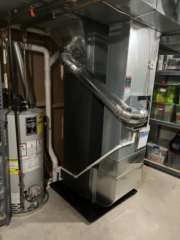 Completed full HVAC system installation including new furnace and air conditioning unit in residential basement utility area. Installed gray metal furnace unit with proper ductwork connections, black air handler with vertical PVC venting, and configured both units on appropriate drain pan for condensate management. All electrical connections, thermostat wiring, air filtration components, and manufacturer safety labels verified and secured per code requirements.
