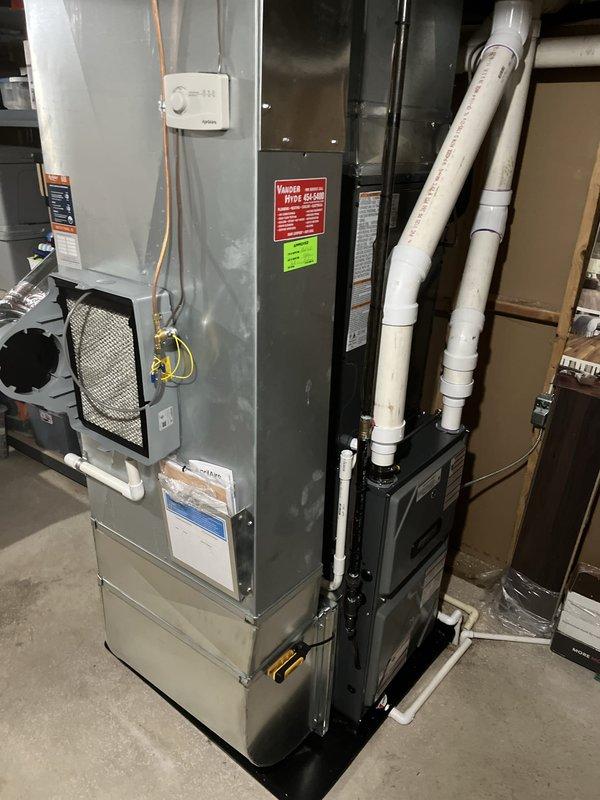 Completed full HVAC system installation including new furnace and air conditioning unit in residential basement utility area. Installed gray metal furnace unit with proper ductwork connections, black air handler with vertical PVC venting, and configured both units on appropriate drain pan for condensate management. All electrical connections, thermostat wiring, air filtration components, and manufacturer safety labels verified and secured per code requirements.