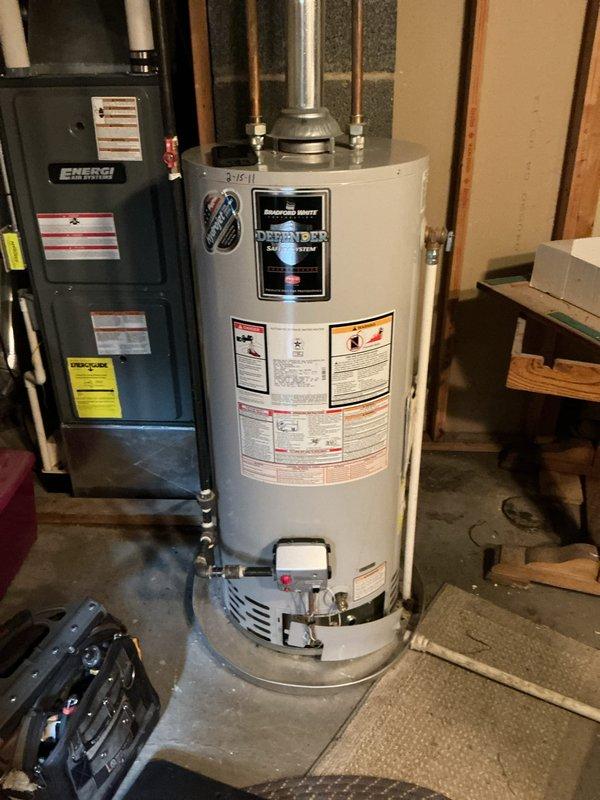 Responded to no hot water complaint on 15-year-old Bradford White water heater. Upon inspection, unit was not producing hot water and had reached end of serviceable life. Documented existing installation with basement utility room setup including gas connections, venting system, and plumbing configuration for replacement recommendations.