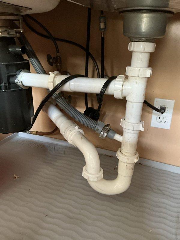 Responded to kitchen sink drain blockage that had persisted for three to four days in a 15-20 year old home. Upon arrival, inspected double-basin stainless steel sink with garbage disposal and dishwasher connection via gray corrugated flexible hose. Examined PVC drain assembly including P-trap and slip-joint fittings under sink. Performed water flow test to verify drainage issue and photographed plumbing configuration showing white PVC pipes, disposal unit, and proper connections. Advised homeowner to continue avoiding dishwasher use until drainage system is fully cleared to prevent backup into sink basin.