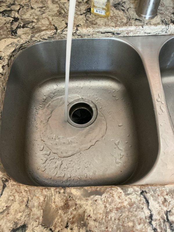 Responded to kitchen sink drain blockage that had persisted for three to four days in a 15-20 year old home. Upon arrival, inspected double-basin stainless steel sink with garbage disposal and dishwasher connection via gray corrugated flexible hose. Examined PVC drain assembly including P-trap and slip-joint fittings under sink. Performed water flow test to verify drainage issue and photographed plumbing configuration showing white PVC pipes, disposal unit, and proper connections. Advised homeowner to continue avoiding dishwasher use until drainage system is fully cleared to prevent backup into sink basin.