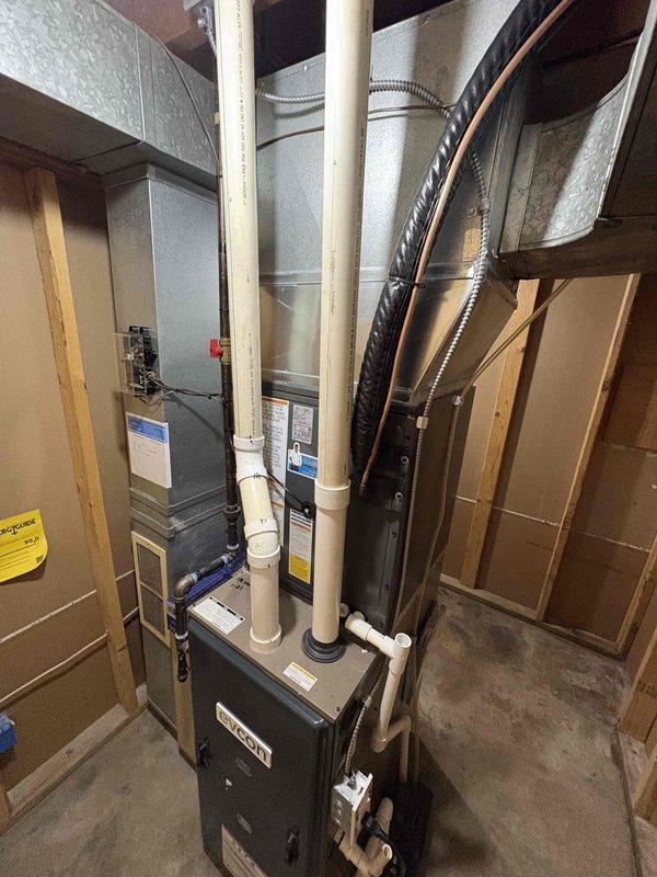 Completed full air conditioning system replacement including outdoor condensing unit and indoor components. Installed new AC unit on concrete pad with proper refrigerant line connections and condensate drainage via white PVC piping routed along exterior siding. Verified all ductwork connections to existing furnace system in basement, ensured proper electrical connections at panel, and tested system operation for optimal cooling performance.