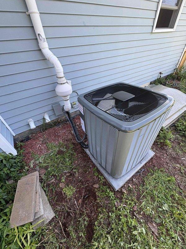 Completed full air conditioning system replacement including outdoor condensing unit and indoor components. Installed new AC unit on concrete pad with proper refrigerant line connections and condensate drainage via white PVC piping routed along exterior siding. Verified all ductwork connections to existing furnace system in basement, ensured proper electrical connections at panel, and tested system operation for optimal cooling performance.