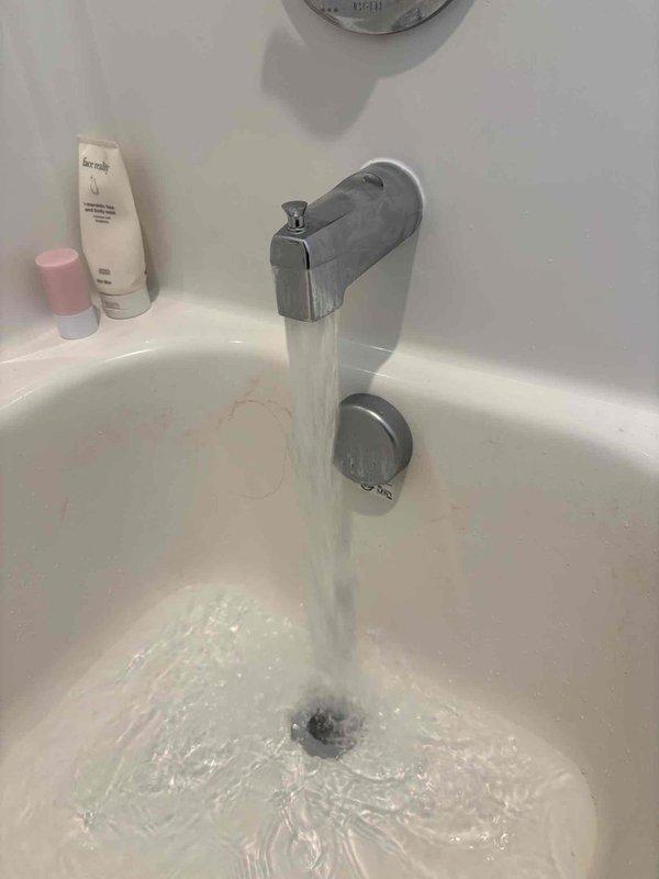 Responded to reported ceiling leak in bathroom of four-year-old single-family home. Upon arrival, conducted visual inspection of affected area and accessed ceiling cavity through existing or created access panel to identify source of moisture intrusion. Inspection revealed plumbing system components, including white PVC piping running vertically through the ceiling space above the bathtub area. Examined bathtub fixtures, including chrome tub spout and associated plumbing connections, to determine potential leak points. Documented conditions with photographs showing active water flow from tub spout and ceiling access point with exposed framing and plumbing infrastructure. Investigation focused on identifying whether leak originated from supply lines, drain connections, or fixture mounting points within the wall and ceiling assembly.