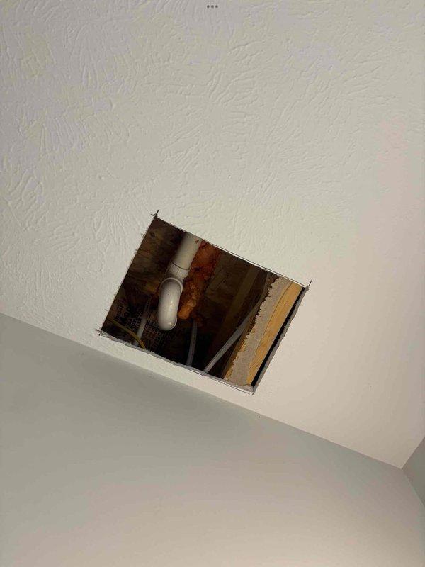 Responded to reported ceiling leak in bathroom of four-year-old single-family home. Upon arrival, conducted visual inspection of affected area and accessed ceiling cavity through existing or created access panel to identify source of moisture intrusion. Inspection revealed plumbing system components, including white PVC piping running vertically through the ceiling space above the bathtub area. Examined bathtub fixtures, including chrome tub spout and associated plumbing connections, to determine potential leak points. Documented conditions with photographs showing active water flow from tub spout and ceiling access point with exposed framing and plumbing infrastructure. Investigation focused on identifying whether leak originated from supply lines, drain connections, or fixture mounting points within the wall and ceiling assembly.