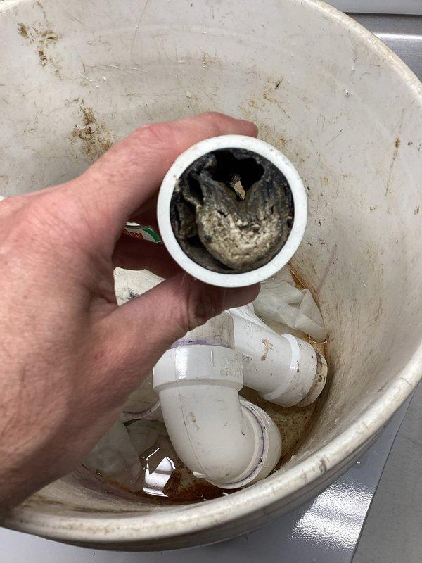 Responded to backup issue with newly installed AC condensate drain line. Removed and cleaned clogged PVC drain fittings that were causing water to back up into the system. Reinstalled proper drainage assembly with P-trap configuration in basement area to ensure adequate flow and prevent future blockages.