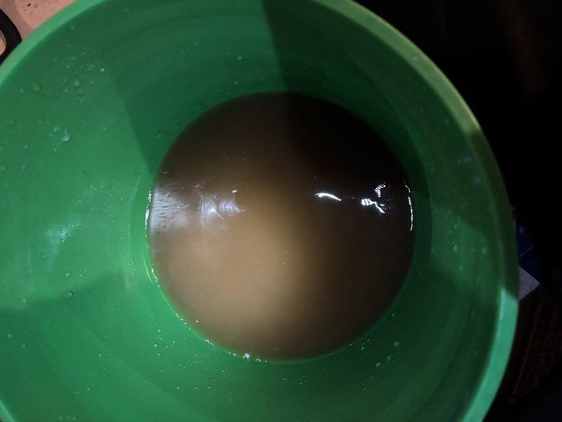 Responded to service call for gas valve issue affecting entire home over several months in four-year-old residence. Upon inspection, discovered severely corroded compressor terminal with heavy white and blue-green crystalline oxidation buildup obscuring original metal finish. Collected water sample from system showing murky brownish-tan discoloration, indicating potential moisture intrusion contributing to electrical component degradation. Documented corrosion damage to terminal post and surrounding wire connections on black plastic base. Photographed affected components and water contamination for service records.